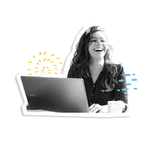 A person with long brown hair smiles widely as they look up from their laptop