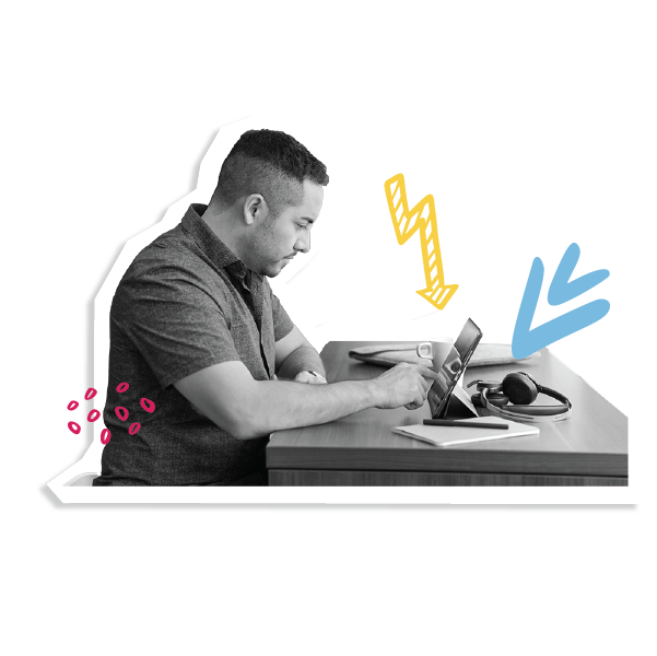 Person working at a desk. They are using a tablet. On the desk is a cup of coffee, a pen and paper and headphones.